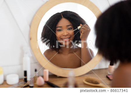 Beauty routines for healthy skin. Black woman applying hydrating serum or hyalurinic acid near mirror at home Beauty routines for healthy skin. Black woman applying hydrating serum or hyalurinic acid near mirror at home 80817341