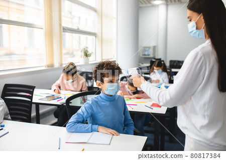 Teacher with contactless thermometer measuring temperature of small boy 80817384