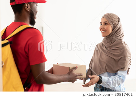 Black delivery man holding box giving it to muslim woman Black delivery man holding box giving it to muslim woman 80817401
