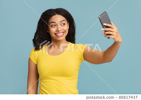 Positive black lady making selfie on smartphone, posing and having fun over blue studio background 80817437