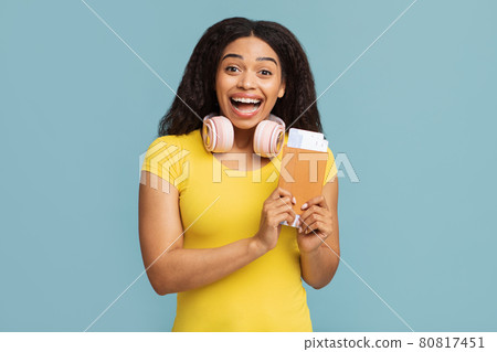 Cheap flights concept. Overjoyed black woman holding passport and boarding pass tickets, standing on blue background Cheap flights concept. Overjoyed black woman holding passport and boarding pass tickets, standing on blue background 80817451
