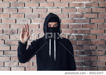 Over a brick wall, a hacker wears a black overcoat. Over a brick wall, a hacker wears a black overcoat. 80822837
