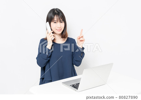 A young woman making a phone call while using a computer 80827890
