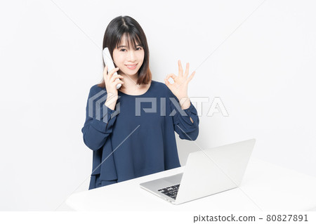 A young woman making a phone call while using a computer 80827891