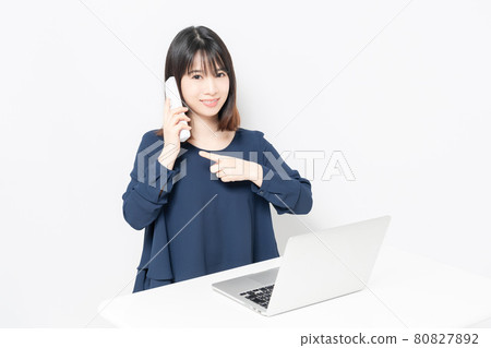 A young woman making a phone call while using a computer 80827892