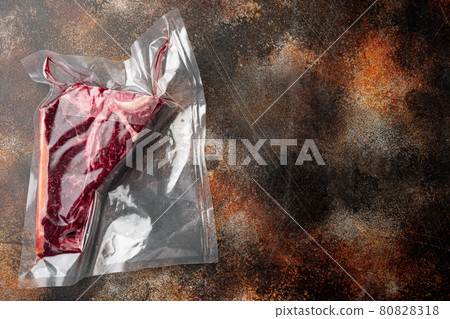 T-bone or florentine dry aged raw marbled beef steak in vacuum packaging, on old dark rustic background, top view flat lay, with copy space for text 80828318