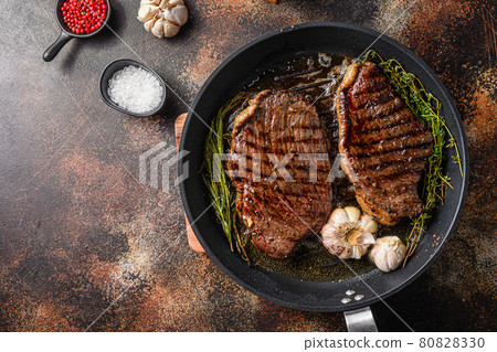 Grilled picanha organic beef steaks on pan with herbs and garlic. Over old dark metall background, top view with space for text. Grilled picanha organic beef steaks on pan with herbs and garlic. Over old dark metall background, top view with space for text. 80828330