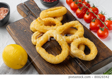 Oven baked breaded calamari rings, on serving board, on white stone table background Oven baked breaded calamari rings, on serving board, on white stone table background 80828342