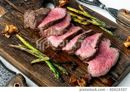 Juicy steak medium rare beef Filet Mignon or Eye Fillet, with onion and asparagus, on wooden serving board, with meat knife and fork, on white stone background 80828387