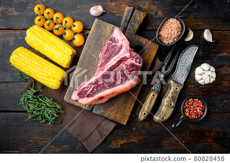 Cooking meat background. Raw aged beef t-bone steak, with spices and herbs for grill, on old dark wooden table background, top view flat lay Cooking meat background. Raw aged beef t-bone steak, with spices and herbs for grill, on old dark wooden table background, top view flat lay 80828458