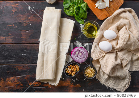 Greek spanakopita ingredients filo spinach eggs feta top view on dark wooden background space for text. Greek spanakopita ingredients filo spinach eggs feta top view on dark wooden background space for text. 80828469