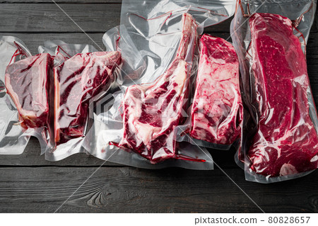 Raw marbled beef steak in vacuum packaging, tomahawk, t bone, club steak, rib eye and tenderloin cuts, on black wooden table background Raw marbled beef steak in vacuum packaging, tomahawk, t bone, club steak, rib eye and tenderloin cuts, on black wooden table background 80828657