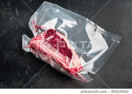 Raw beef meat Club or striploin on the bone steak in plastic airtight pack, on black stone background, with copy space for text 80828692