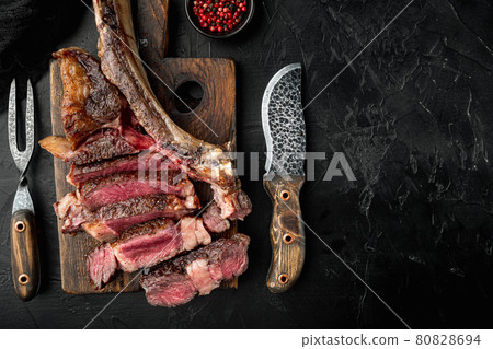 Grilled sliced tomahawk beef steak, on wooden serving board, on black stone background, top view flat lay 80828694