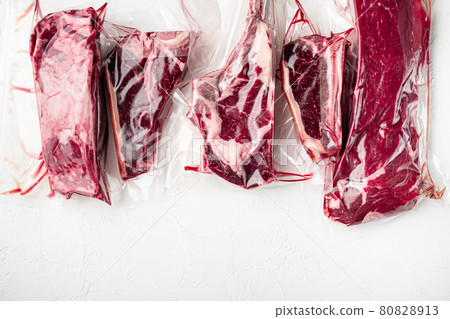 Vacuum packed organic raw beef classic cuts, tomahawk, t bone, club steak, rib eye and tenderloin cuts, on white stone background, top view flat lay, with copy space for text Vacuum packed organic raw beef classic cuts, tomahawk, t bone, club steak, rib eye and tenderloin cuts, on white stone background, top view flat lay, with copy space for text 80828913
