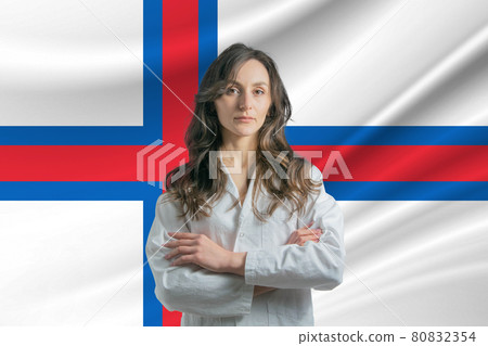 Medicine in Faroe Islands. Happy beautiful female doctor in medical coat standing with crossed arms against the background of the flag of Faroe Islands Medicine in Faroe Islands. Happy beautiful female doctor in medical coat standing with crossed arms against the background of the flag of Faroe Islands 80832354