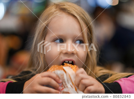 Little girl eating burger in fast food cafe Little girl eating burger in fast food cafe 80832843