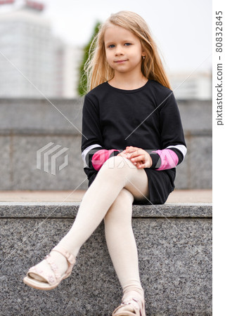 Little girl in a black dress sits on a bench 80832845