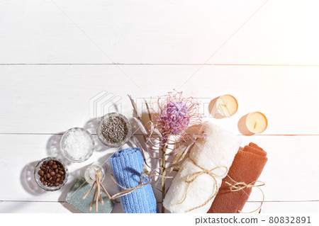 Spa products. Bath salts, dry flowers lavender, soap, candles and towel. Flat lay on white wooden background, top view. Sun flare 80832891