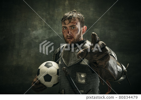 Portrait of one brutal bearded man, medeival warrior or knight with dirty wounded face holding ball on dark background. 80834479