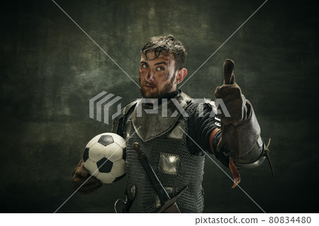 Portrait of one brutal bearded man, medeival warrior or knight with dirty wounded face holding ball on dark background. 80834480