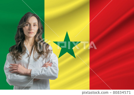Medicine in Senegal. Happy beautiful female doctor in medical coat standing with crossed arms against the background of the flag of Senegal 80834571