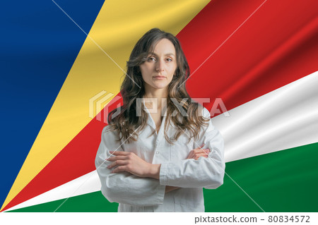 Medicine in Seychelles. Happy beautiful female doctor in medical coat standing with crossed arms against the background of the flag of Seychelles 80834572