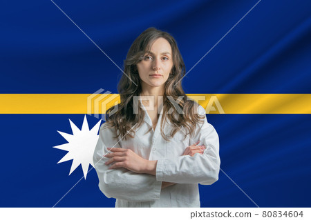 Medicine in Nauru. Happy beautiful female doctor in medical coat standing with crossed arms against the background of the flag of Nauru 80834604