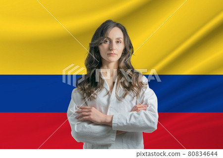 Medicine in Colombia Happy beautiful female doctor in medical coat standing with crossed arms against the background of the flag of Colombia 80834644