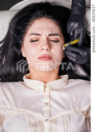 Brunette girl in cosmetology office during plasmolifting procedure lying with closed eyes 80834817