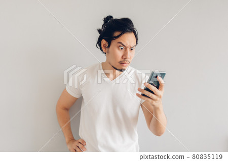 Serious long hair man in white casual t-shirt is using smartphone. 80835119
