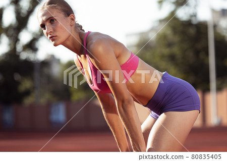 One Caucasian woman, female athlete, runner training at public stadium, sport court or palyground outdoors. Summer sport games. One Caucasian woman, female athlete, runner training at public stadium, sport court or palyground outdoors. Summer sport games. 80835405