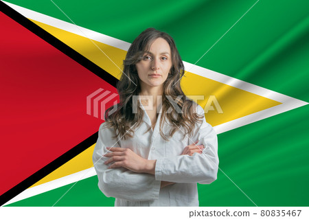 Medicine in Guyana. Happy beautiful female doctor in medical coat standing with crossed arms against the background of the flag of Guyana Medicine in Guyana. Happy beautiful female doctor in medical coat standing with crossed arms against the background of the flag of Guyana 80835467