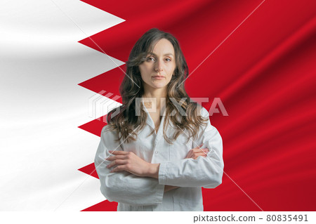 Medicine in Bahrain. Happy beautiful female doctor in medical coat standing with crossed arms against the background of the flag of Bahrain 80835491