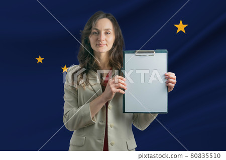 Study in Alaska. Beautiful woman holding a sheet of paper in her hands. Girl on the background of the flag of Alaska Study in Alaska. Beautiful woman holding a sheet of paper in her hands. Girl on the background of the flag of Alaska 80835510