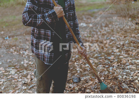 Gardening concept a male gardener using a coconut-leaf broom gathering the dry fallen leaves for cleaning the area 80836198