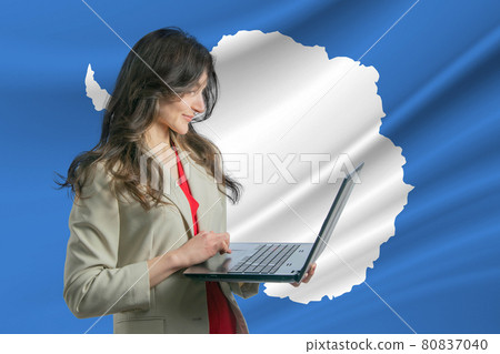 Freelance in Antarctica. Beautiful young woman freelancer uses laptop computer against the background of the flag of Antarctica 80837040