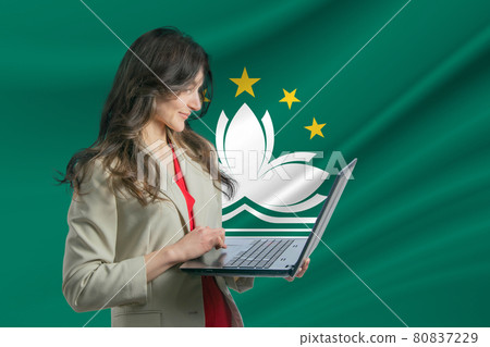 Freelance in Macau. Beautiful young woman freelancer uses laptop computer against the background of the flag of Macau Freelance in Macau. Beautiful young woman freelancer uses laptop computer against the background of the flag of Macau 80837229