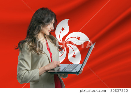Freelance in Hong Kong. Beautiful young woman freelancer uses laptop computer against the background of the flag of Hong Kong Freelance in Hong Kong. Beautiful young woman freelancer uses laptop computer against the background of the flag of Hong Kong 80837230