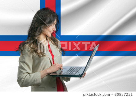 Freelance in Faroe Islands. Beautiful young woman freelancer uses laptop computer against the background of the flag of Faroe Islands Freelance in Faroe Islands. Beautiful young woman freelancer uses laptop computer against the background of the flag of Faroe Islands 80837231