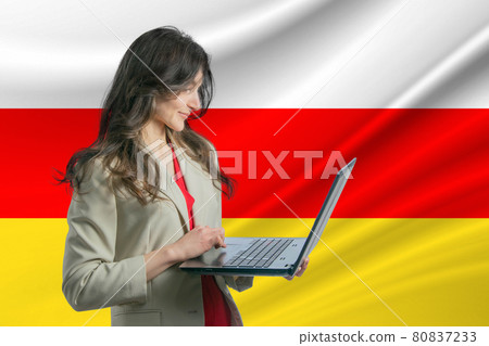 Freelance in South Ossetia. Beautiful young woman freelancer uses laptop computer against the background of the flag of South Ossetia Freelance in South Ossetia. Beautiful young woman freelancer uses laptop computer against the background of the flag of South Ossetia 80837233
