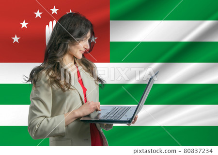 Freelance in Abkhazia. Beautiful young woman freelancer uses laptop computer against the background of the flag of Abkhazia Freelance in Abkhazia. Beautiful young woman freelancer uses laptop computer against the background of the flag of Abkhazia 80837234
