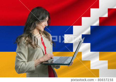 Freelance in Nagorno-Karabakh Republic. Beautiful young woman freelancer uses laptop computer against the background of the flag of Nagorno-Karabakh Republic 80837238