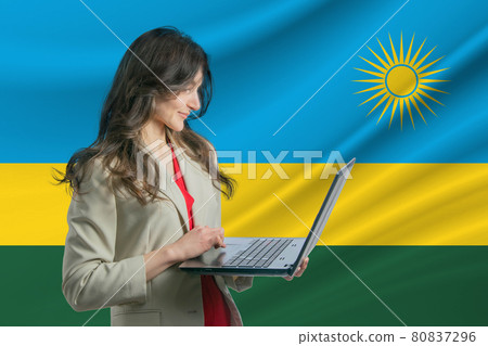 Freelance in Rwanda. Beautiful young woman freelancer uses laptop computer against the background of the flag of Rwanda Freelance in Rwanda. Beautiful young woman freelancer uses laptop computer against the background of the flag of Rwanda 80837296