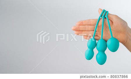 A faceless woman demonstrates a set of mint-colored vaginal balls. Girl holding a kegel trainer for training pelvic floor muscles on a white background. A faceless woman demonstrates a set of mint-colored vaginal balls. Girl holding a kegel trainer for training pelvic floor muscles on a white background. 80837866