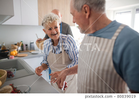Senior couple with friends having party indoors, talking when cooking. Senior couple with friends having party indoors, talking when cooking. 80839019