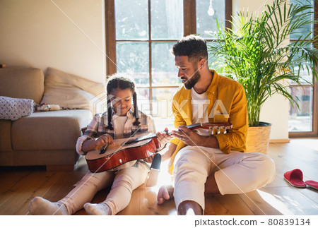 Front view of small girl with adult brother indoors at home, playing guitar. Front view of small girl with adult brother indoors at home, playing guitar. 80839134
