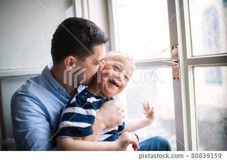 Father with happy down syndrome son indoors at home, kissing his cheek. 80839159