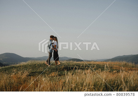 Young couple on a walk in nature at sunset in countryside, kissing. 80839578