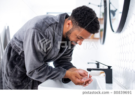 Young man washing face indoors at home, morning or evening routine concept. Young man washing face indoors at home, morning or evening routine concept. 80839691